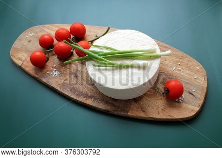 Homemade Goats Milk Cheese, Small Tomatoes On A Branch, Red Sauce On A Wooden Board On A Dark Green 