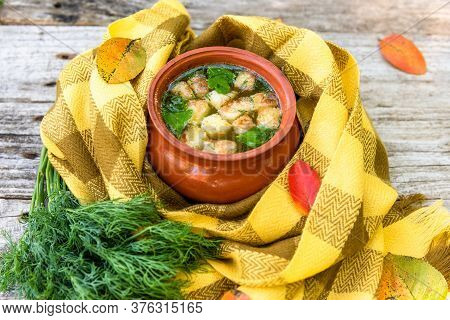 Soup With Croutons And Dill In A Clay Pot Wrapped In A Checkered Yellow Scarf For Warmth And Strewn 
