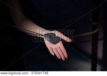 An Unrecognizable Woman Demonstrates An Elegant Thin Leather Strip Whip In A Dark Bedroom. Close-up 