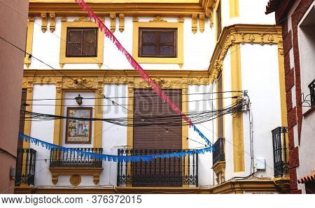 Historic House Facade With Yellow Stucco And Tile Painting Of Siant Francesco Assisi And Colorful Fl
