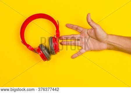 Hand Holding Red Headphones On Yellow Background. Music Concept