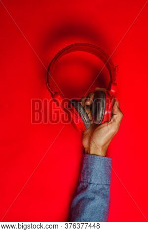 Hand Holding Red Headphones On Red Background. Music Concept