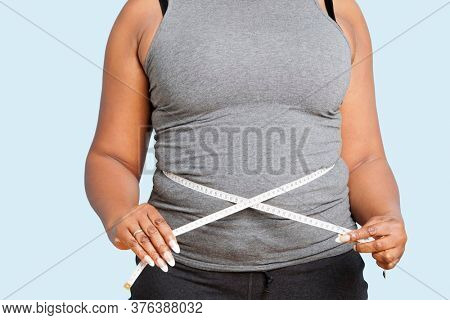 Mid section of woman measuring waist over blue background