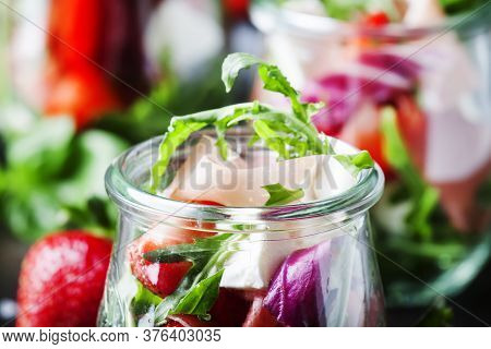 Summer Salad With Arugula, Soft Cheese, Red Strawberry And Prosciutto In Glass Jars On Black Table, 