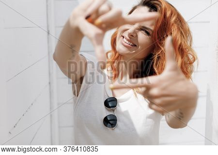 Possitive Redhead Woman In Sunglasses Doing Frame Outdoors On White Background