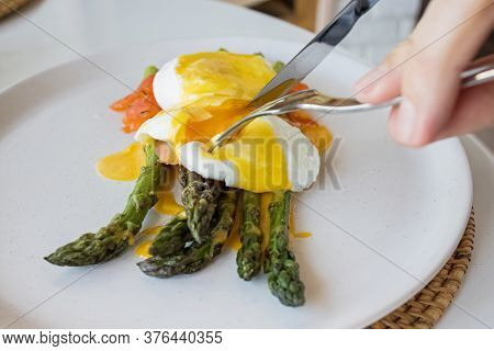 Mans Hands Cutting Poached Egg With Hollandaise Sauce And Salmon Over Asparagus