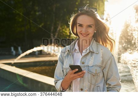 The Glad Girl With Phone. The Girl Gets A Plessure Message. The Attractive Girl Is In Sunlight.