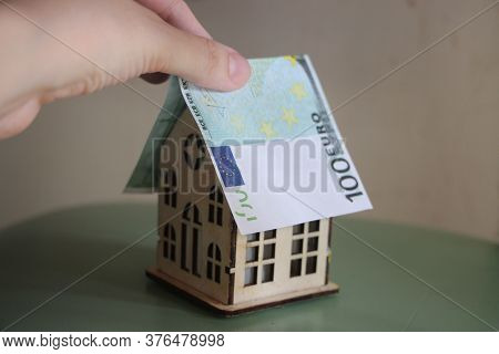 Hand Puts Euro Bill Like Roof On Toy House. Buying Property Re Business Concept