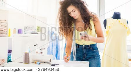 Cute dressmaker overwriting from phone in light atelier