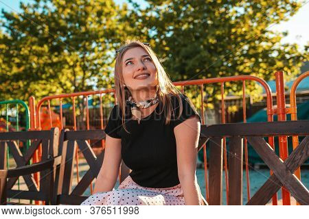 Portrait Of A Pretty Young Woman Is Sitting On A Park Bench And Looking Up At The Sky With A Dreamy 