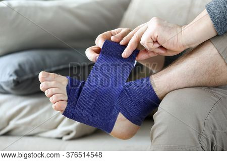 Man Sits At Home Couch And Bandages Foot Bandage. Uniform Compression All Areas For Foot Massage Eff