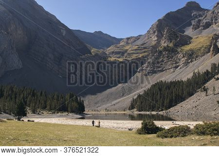 Ibon De Plan Lake Surrounded By High Mountains And Some Bikers In Pyrenees In Huesca Spain