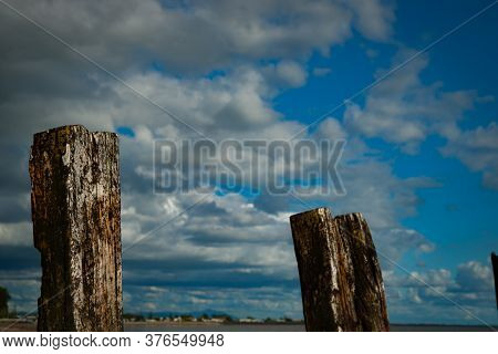 Two Old Pier Posts Below Cloudy Sky.