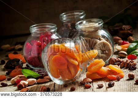 Dried Apricots In A Glass Jar On A Dark Wooden Background With Crumbled Nuts And Dried Fruits, Selec