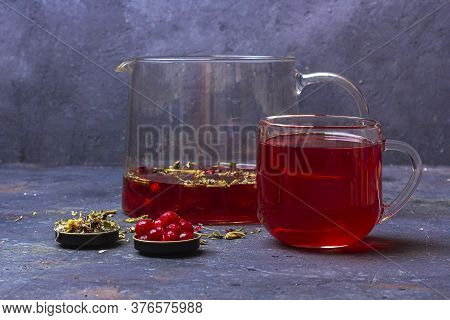 Red Tea (rooibos, Hibiscus, Karkade) In Glass Cup And Teapot Among Dry Tea Leaf, Petals And Cranberr