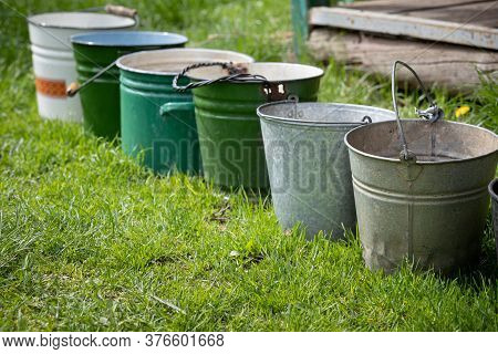 Several Old Buckets Are Standing On The Grass In Sunny Weather. Collecting Rainwater In Buckets In T