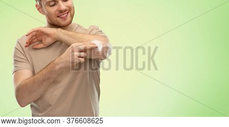 health problem and people concept - happy smiling young man applying pain medication or moisturizing cream to his elbow over lime green natural background