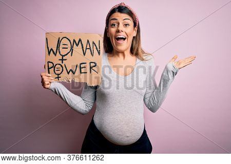 Young brunette woman pregnant expecting baby holding banner asking for women power very happy and excited, winner expression celebrating victory screaming with big smile and raised hands