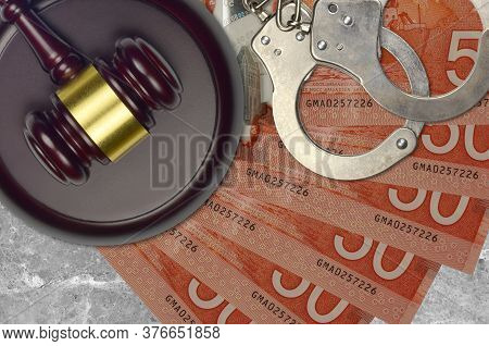 50 Canadian Dollars Bills And Judge Hammer With Police Handcuffs On Court Desk. Concept Of Judicial 