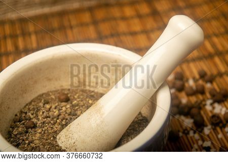 Ground Black In A Ceramic Mortar And Black And Coarse Salt Scattered On A Reed Mat. Close Up.