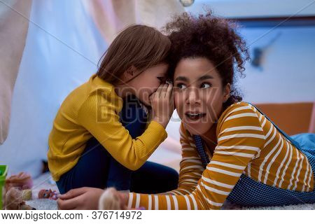 African American Woman Baby Sitter Entertaining Caucasian Cute Little Girl. They Are Gossiping And T