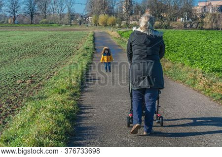 Grandmother With Grandson While Walking And Pushes A Baby Carriage.