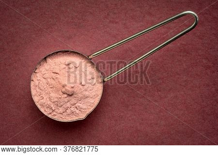 measuring scoop of pomegranate fruit powder - top view against handmde paper, superfood concept
