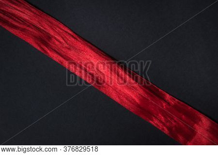 Red Ribbon On A Black Background. The Tape Runs Diagonally From One Corner To The Other.