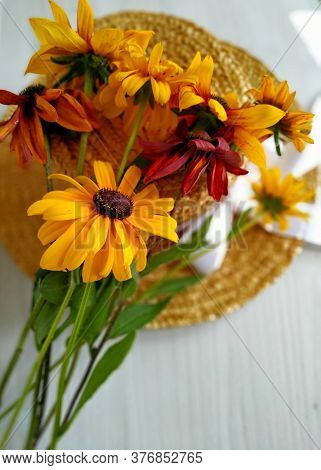Golden Bicolor Rudbeckia Lies On A Wicker Straw Hat On A Light Wood Background. Selective Focus