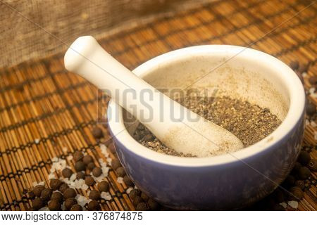 Ground Black In A Ceramic Mortar And Black And Coarse Salt Scattered On A Reed Mat. Close Up.