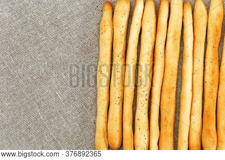 Background Of Breadsticks Stacked In Rows And Sackcloth. Long Bread Sticks Made Of Wheat Flour Lie O