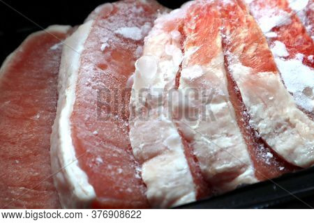 Sliced Frozen Pieces Of Meat. There Are Pieces Of Ice On The Pieces Of Meat. Meat In A Black Plastic