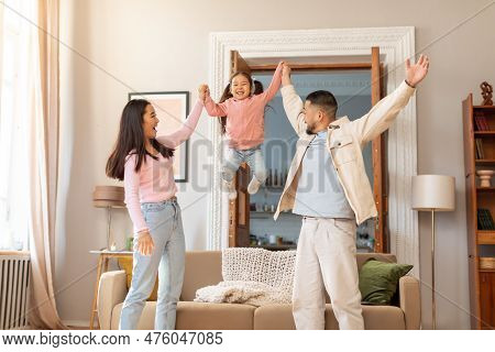 Joyful Parents Holding Hands Lifting Up Little Baby Daughter Indoors