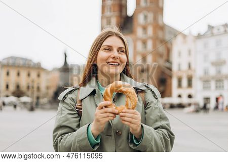 Attractive Young Female Tourist Is Holding Prezel, Traditional Polish Snack On The Market Square In 