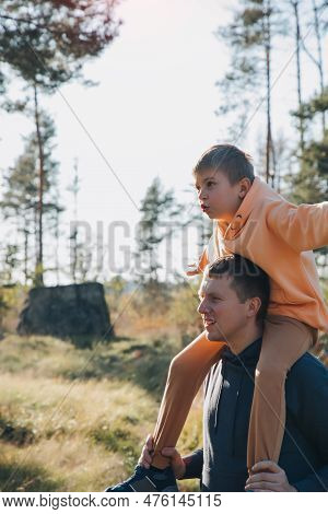 Dad And Son On A Walk In The Forest In Sunny Weather. Family Leisure. The Father Carries His Son On 