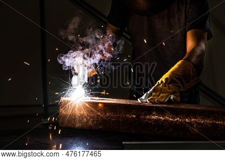 Metal Welder Working With Arc Welding Machine To Weld Steel At Factory While Wearing Safety Equipmen