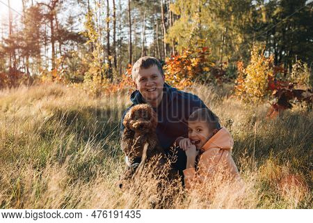 Dad With His Son And A Small Brown Dog Are Playing In A Meadow With Tall Grass. Family Leisure With 