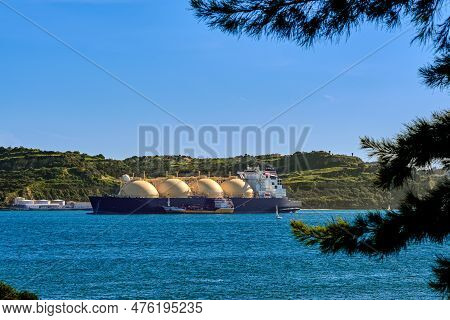 LNG or liquified natural gas tanker moored by industrial pier and green hill on sunny day. Alternative gas supply, commercial freight, energy crisis, regasification, diversification, fuel and energy generation.