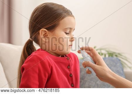 Mother Using Nasal Spray To Treat Her Little Daughter On Sofa Indoors, Closeup