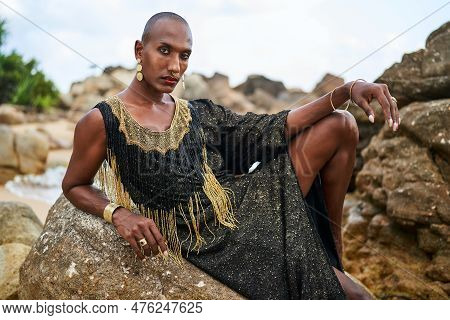 Non-binary Black Person In Luxury Dress On Rocks In Ocean. Trans Ethnic Fashion Model Wearing Jewell