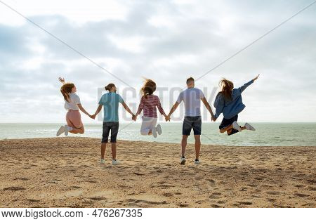 Happy Millennial European And Arab Friends Have Fun, Enjoy Free Time, Jump, Freeze In Air On Ocean B