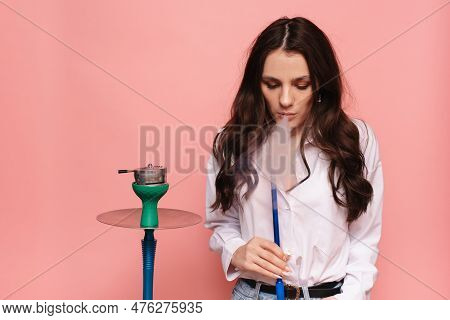 Young, Attractive Woman Smokes A Hookah, Sheesha On A Pink Background. The Pleasure Of Smoking.