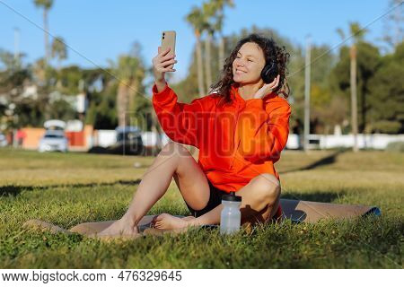 Young Smiling Sportswoman In Wirelles Headphones Listening Music And Using Cellphone During Workout 