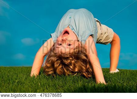 Happy Boy Doing A Headstand On The Grass In The Summer Sunshine. Funny Happy Little Child Standing O