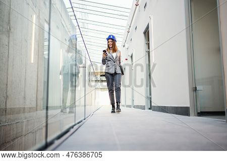 Young Attractive Female Architect Walking Around Building In Construction Process And Reading An E-m