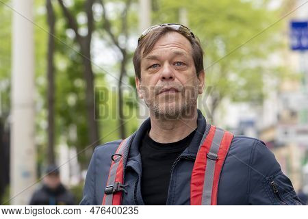 An Elderly Handsome Man Of 50-55 Years On A Blurry Urban Background, Street Portrait 21.