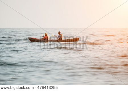 Happy Couple Kayaks In An Inflatable Kayak On The Sea At Sunset. Couple Kanoeing In The Sea Near The