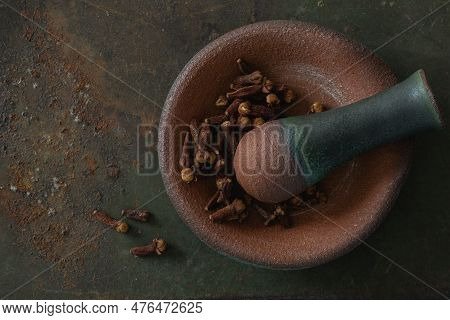 Closeup Top View Of A Small Clay Mortar Dish With A Pestle And Dried Cloves, On Textured Rusted Gree