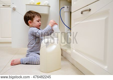 A Child Is Playing With Chemical Cleaning Products Under The Sink In The Kitchen. Baby Holds Bottles