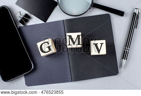 Word Gmv On A Wooden Block On Black Notebook With Smartpone, Credit Card And Magnifier